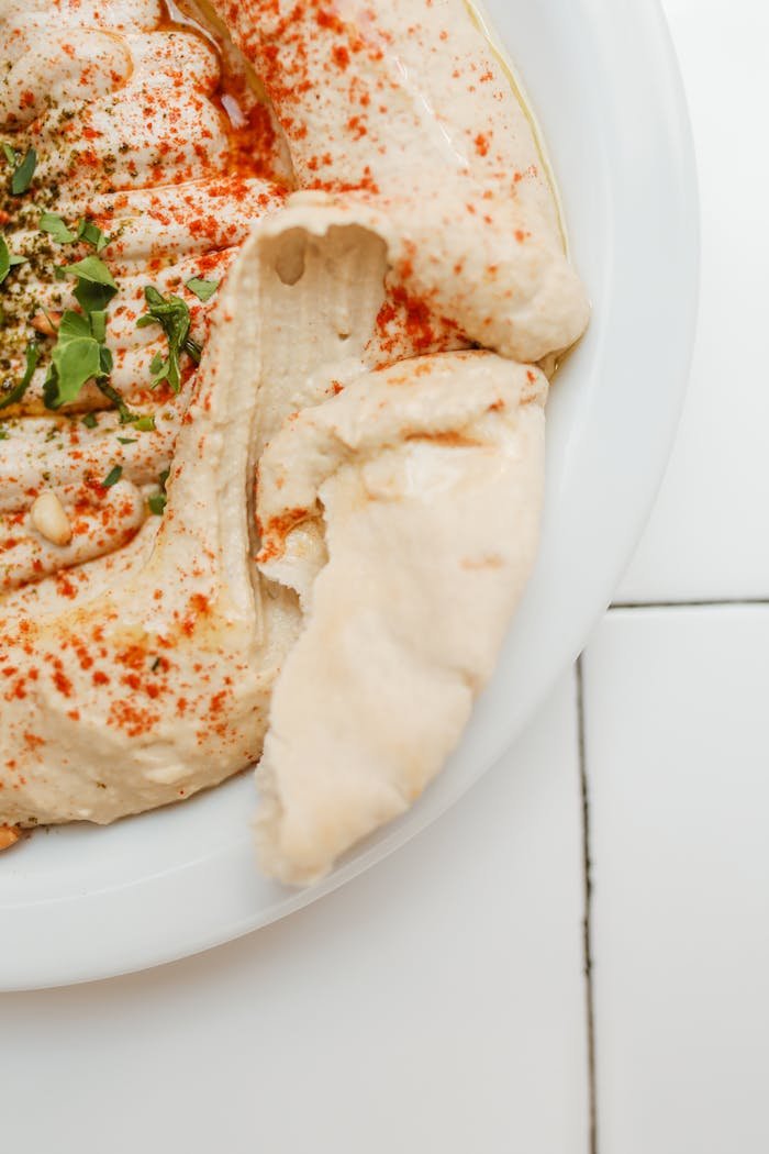 A delicious plate of creamy hummus topped with paprika and fresh herbs, served with pita bread.