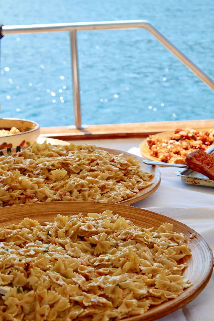 Farfalle pasta served on a boat in Milos, Greece, with a scenic ocean view.